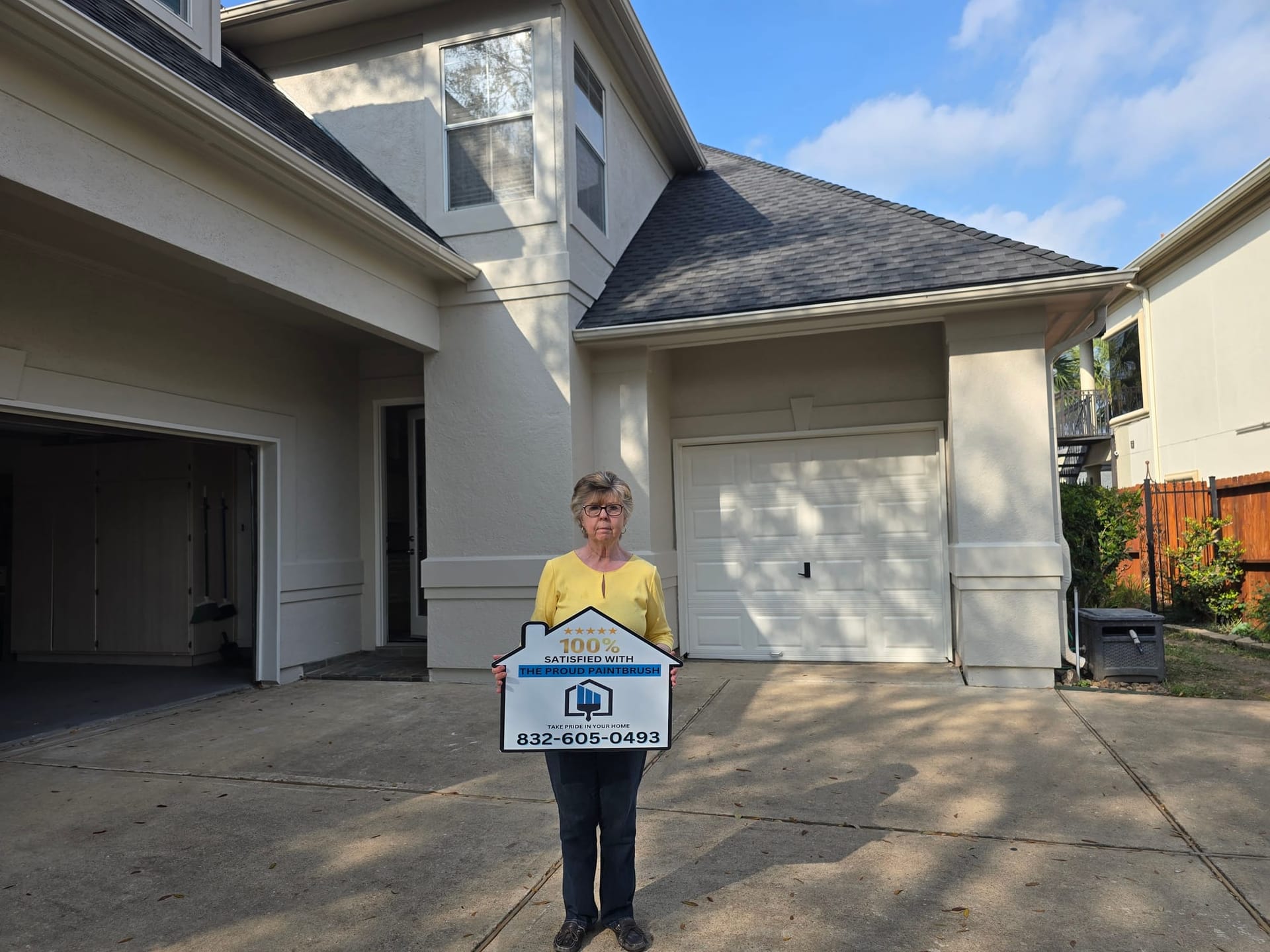 Satisfied customer holding a 100% satisfied sign in front of a freshly painted home in Sugar Land, TX
