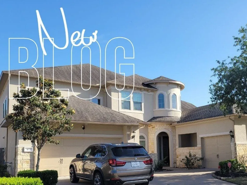 Front view of a large beige house with a driveway, a silver car parked in front, two trees, and a clear blue sky. The words 'New Blog' are overlaid on the image.