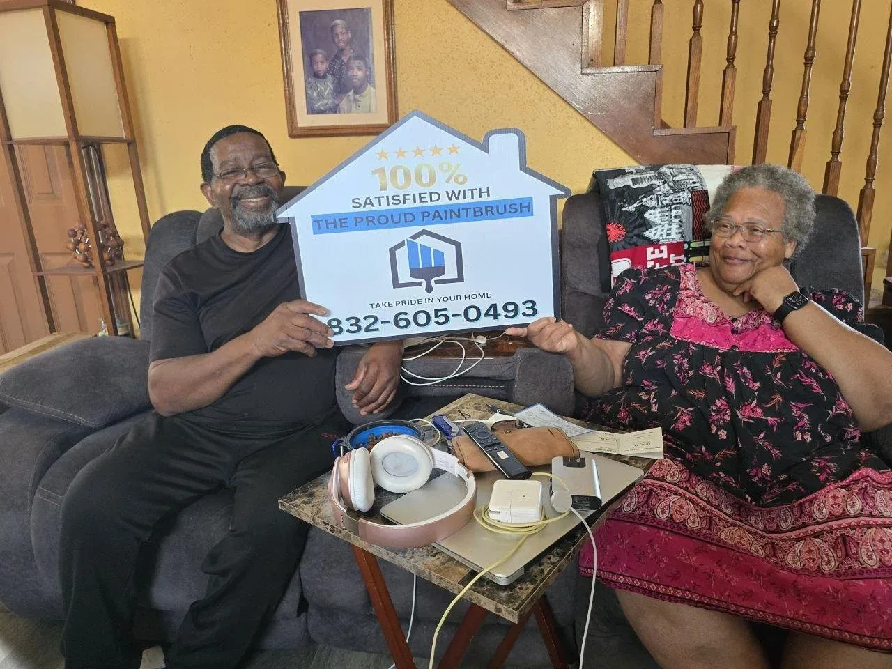 Satisfied Sugar Land homeowners with The Proud Paintbrush sign after exterior painting service.