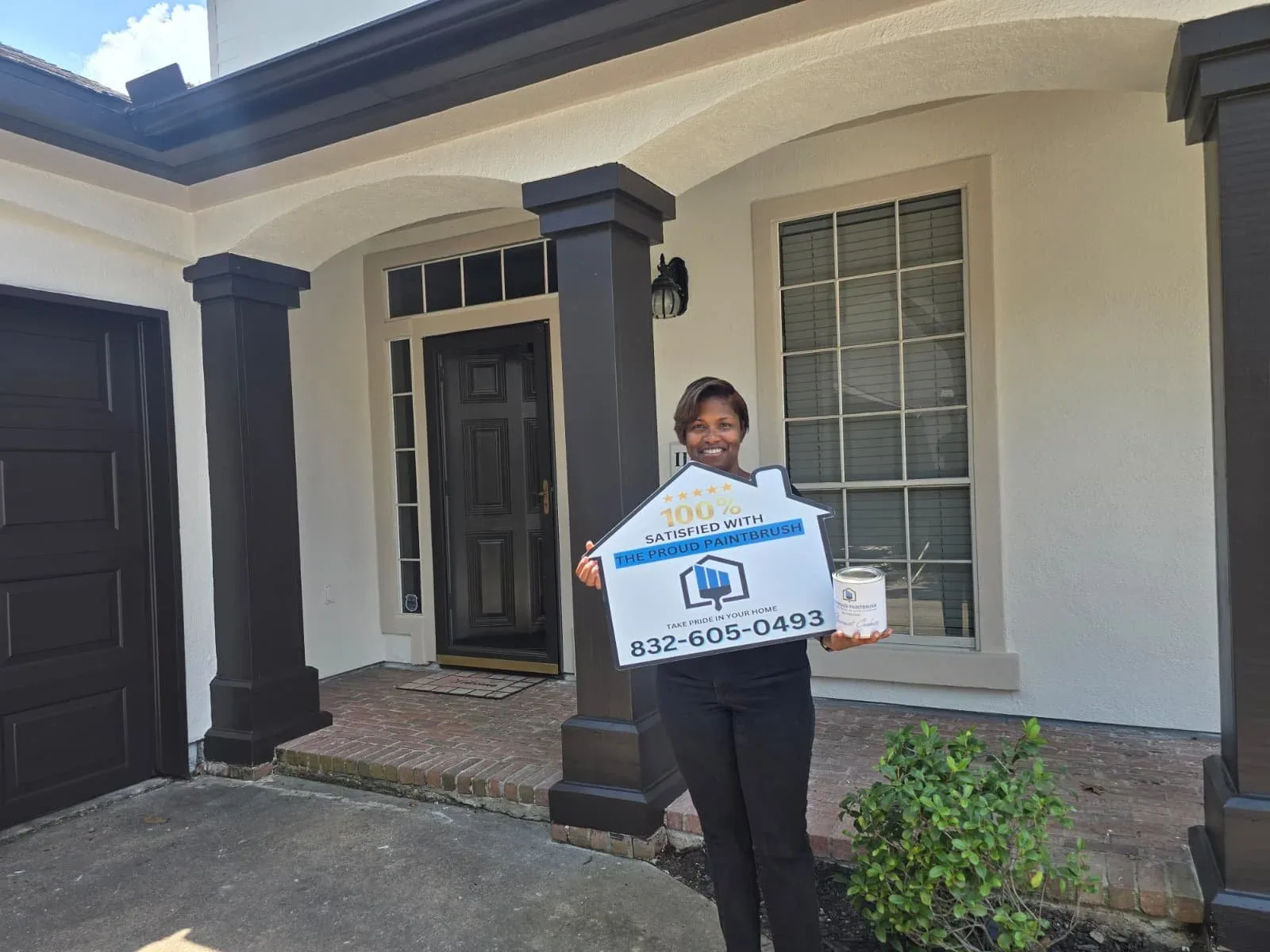 Happy Fulshear, TX homeowner holding a 100% Satisfied sign in front of her freshly painted stucco home by The Proud Paintbrush