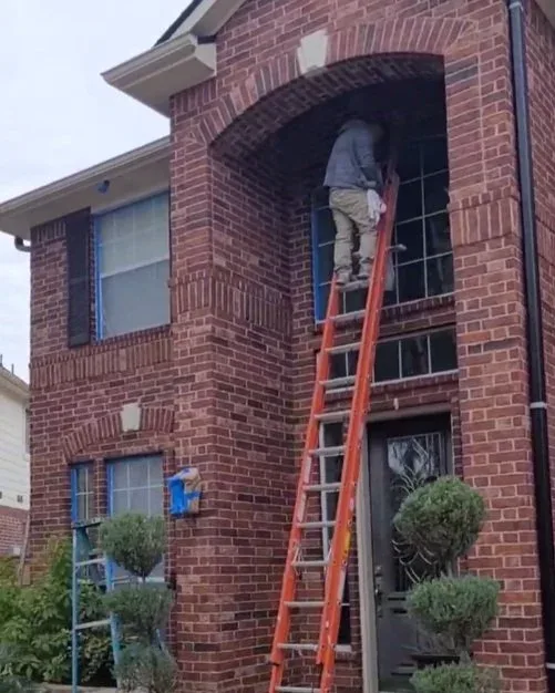 man on ladder masking off window preparing to paint brick house