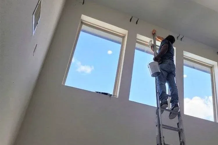 Professional painter on a ladder cutting in paint lines in a two-story living room in Richmond, Texas.