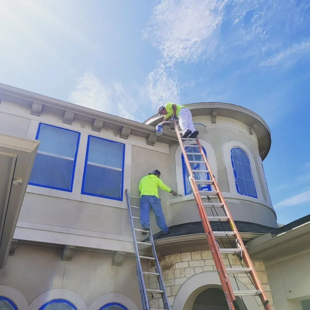 Two painters working on a stucco exterior in Sugar Land by The Proud Paintbrush