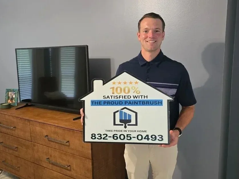 Happy homeowner holding satisfaction sign after bedroom painting project in Richmond, TX by The Proud Paintbrush.