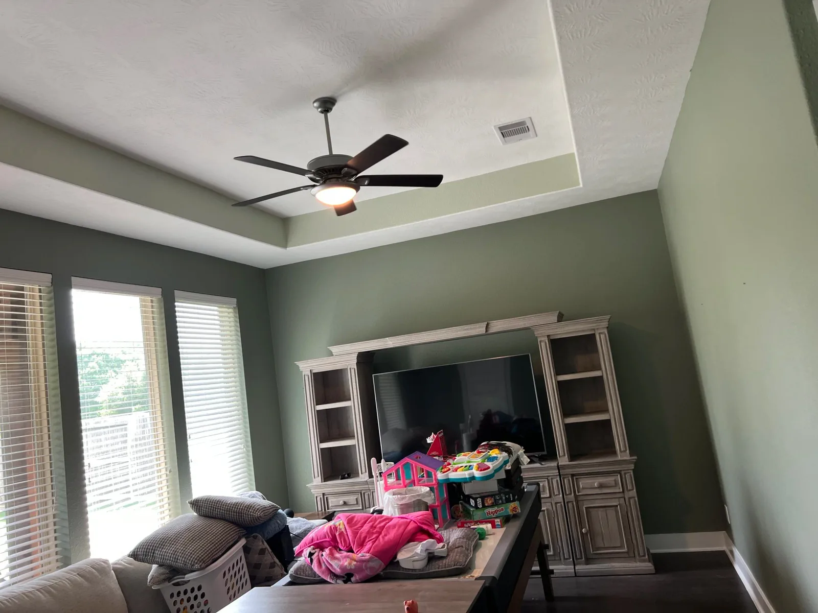 Bedroom with soft green monochromatic paint palette and tray ceiling in Sugar Land, TX interior painting project by The Proud Paintbrush.